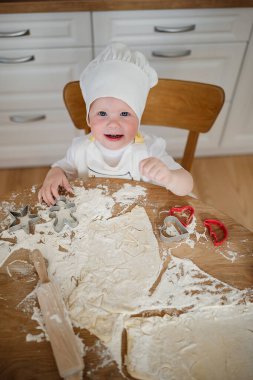 Şef şapkası takan neşeli bir çocuk, un ve kurabiye kesicilerle çevrili güneşli bir mutfakta yemek pişirmekten hoşlanıyor..
