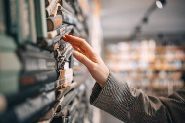 A hand reaches out to touch the spine of a book in a bookshelf, the rest of the bookstore is blurred out in the background. clipart