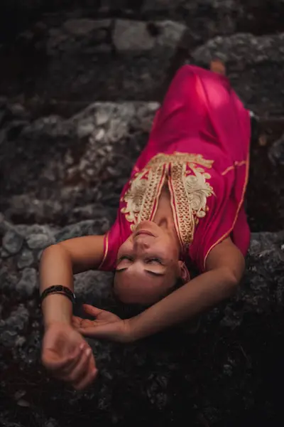 stock image A woman in a vibrant pink outfit lying on ancient rocky ground, enjoying the tranquility of her surroundings at dusk.