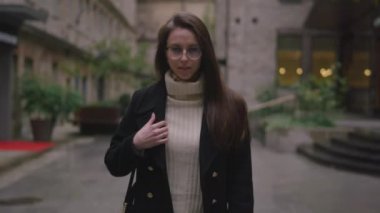 Modern binalarla çevrili tuhaf bir kaldırım taşı yolu boyunca siyah bir ceketle zarif bir şekilde gezinen bir kadın..