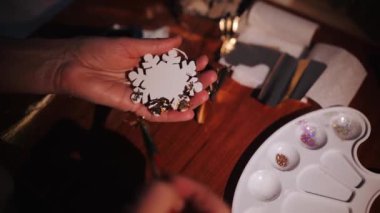 Nazik bir kar tanesinin üzerine ihtişamlı aksanlar yerleştiren ellerin yakından görüntüsü festival sezonuna ışıltı katıyor..