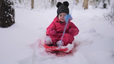 Parlak kırmızı bir kar elbisesi içindeki genç bir çocuk, karlı bir yolda sürüklenirken mutlu bir şekilde kayar..