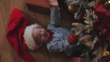 Noel ağacının altında Noel Baba şapkası takmış neşeli küçük bir çocuğun portresi.. 