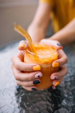 Güneş ışığı altında renkli tırnak sanatı sergileyen bir insan iki elinde de canlı bir portakal suyu tutar..