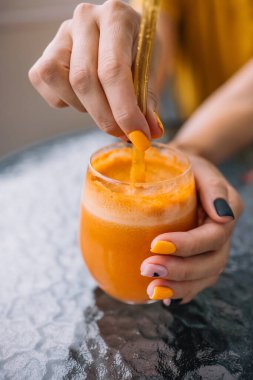 Güneş ışığı altında renkli tırnak sanatı sergileyen bir insan iki elinde de canlı bir portakal suyu tutar..