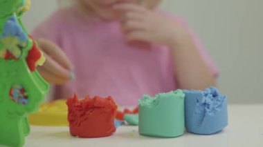 Pembe tişörtlü bir çocuk renkli modelleme kilini manipüle eder, oyun sırasında yaratıcılığı teşvik eder..