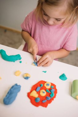 A child passionately molds vibrant play dough into creative shapes and figures on a table. clipart