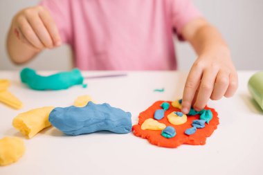 Genç bir çocuk parlak oyun hamuru kullanarak masadaki rengarenk şekilleri şekillendiriyor, yaratıcı oyunlarla meşgul..