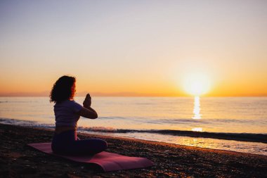 Carefree woman sitting in yoga mountain pose by the sea sunrise time. Finding inner peace spiritual healing lifestyle. Stretching in the morning for increasing energy.