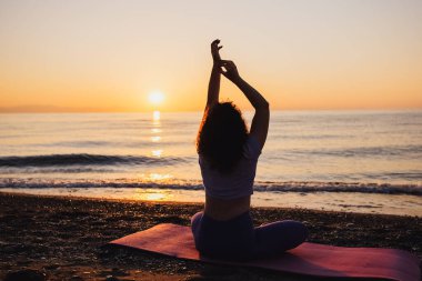 Backside view of calm woman yoga practicing by the sea sunrise time. Finding inner peace spiritual healing lifestyle.
