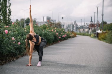 Bir kadın, şehir ortamında çiçeklerle çevrili asfalt bir yolda yoga pozu veriyor..