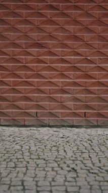Kalıplaşmış kırmızı tuğla duvar geometrik desenler içerir, sanatsal bir kentsel zemin oluşturur.