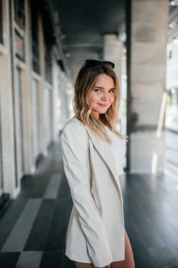 Pretty woman in white jacket posing on modern city street. 