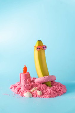 Eğlenceli bir kumsal düzeneği pembe güneş gözlüğü takan bir muza ev sahipliği yapar. Pembe kum ve mumla çevrili..