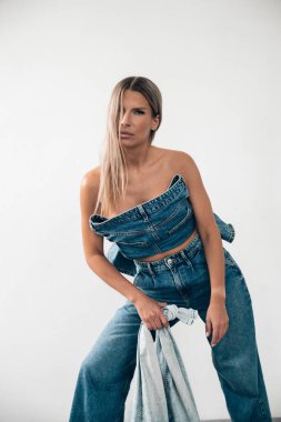 Bir model şık bir kot elbise sergiliyor, basit bir ortama özgüvenle cesur bir poz veriyor..