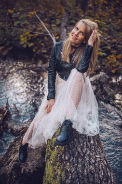 Genç bir kadın, sonbahar yaprakları arasında sakin bir ifadeyle bir kütüğün üzerinde oturarak doğanın tadını çıkarır..