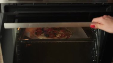 Ev yapımı pizzayı fırına koyan biri. Evde yemek pişirmek.