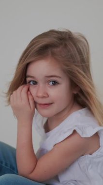 Neşeli genç bir kız otururken saçlarıyla oynar ve gülümser, neşeli ruhunu ve günlük kıyafetlerini gösterir..