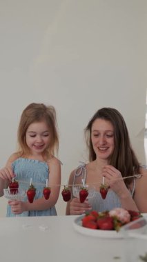Bir anne ve kızı mutlu bir şekilde şeker kaplı çilekler hazırlıyor, birlikte gülüyor ve eğleniyorlar..