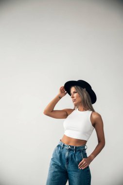 Beyaz bir bluz ve kot giyen genç bir kadın zarif bir poz veriyor, kendine güvenini ve tarzını gösteriyor..