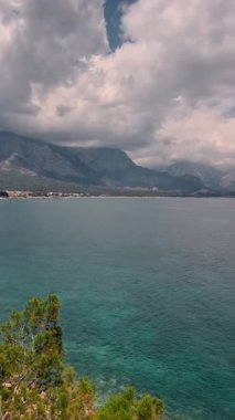 Berrak suların, uzak dağların ve dramatik bulutların olduğu sakin bir kıyı manzarasının tadını çıkar..