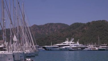 Gocek - Fethiye, Türkiye - 10 Mayıs 2025: Güneşli bir günde dağlarla çevrili bir marinada demirlemiş lüks yatların çarpıcı manzarasının tadını çıkarın.