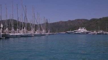 Gocek - Fethiye, Türkiye - 10 Mayıs 2025: Kayıkçılar, tepelerle çevrili yelkenli ve lüks yatlarla dolu güneşli bir marinada güneşli bir günün tadını çıkarıyorlar.