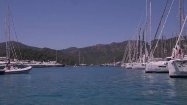 Gocek - Fethiye, Türkiye - 10 Mayıs 2025: Arka planda dağlar ve tepede parlak güneş ışığıyla sakin bir marinada birden fazla tekne yüzüyor.