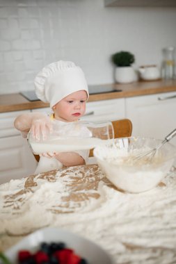 Şef şapkalı küçük bir çocuk dikkatlice karıştırma kabına süt dökerek mutfakta lezzetli bir karmaşa yaratıyor..