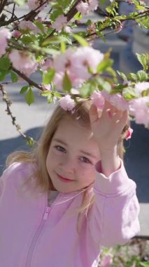 Genç bir kız halka açık bir parkta güneşli bir bahar gününde güzel pembe kiraz çiçeklerinin altında oynar..