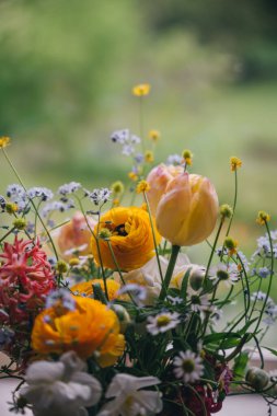 Laleler ve papatyalar da dahil olmak üzere renkli çiçekler arka planda yeşillik olan bir yüzey üzerinde güzelce düzenlenmiştir..