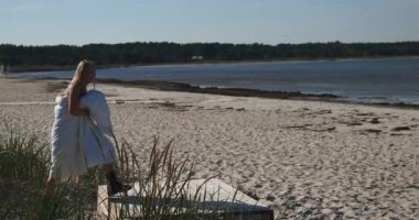 Beyaz battaniyeli mutlu sarışın kadın kumlu bir sahilde havaya zıplıyor.. 