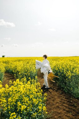 Beyaz giyinmiş bir insan, parlak sarı çiçeklerle dolu bir tarlada güneşli bir öğleden sonranın tadını çıkarıyor..