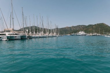 Gocek - Fethiye, Türkiye - 10 Mayıs 2025: Lüks yatlar, açık mavi gökyüzünün altındaki yeşil tepelerle çevrili sakin bir marinaya demirlediler.