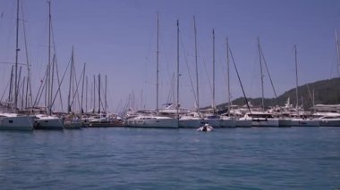 Gocek - Fethiye, Türkiye - 10 Mayıs 2025: Arka planda dağlar ve tepede parlak güneş ışığıyla sakin bir marinada birden fazla tekne yüzüyor.