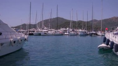 Gocek - Fethiye, Türkiye - 10 Mayıs 2025: Arka planda dağlar ve tepede parlak güneş ışığıyla sakin bir marinada birden fazla tekne yüzüyor.