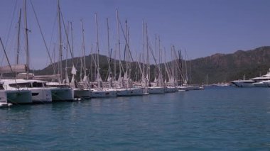 Gocek - Fethiye, Türkiye - 10 Mayıs 2025: Arka planda dağlar ve tepede parlak güneş ışığıyla sakin bir marinada birden fazla tekne yüzüyor.