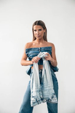 Bir model, minimalist bir stüdyoda, kot elbise giyer ve ceket giyer..