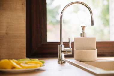 Parlak mutfak pencerenin yanındaki tezgahta parlak bir musluk, taze dilimlenmiş limon ve limonlar var..