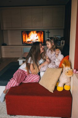 Bir anne ve kızı, aynı pijamaları giyerken şöminenin yanında keyifli bir şekilde vakit geçirirler..