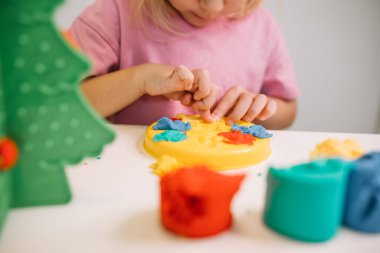 Genç bir çocuk, kapalı bir alanda parlak, renkli oyun hamuru kalıbına konsantre olur..