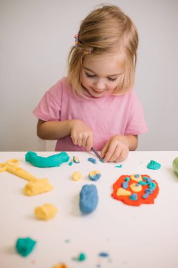 Bir çocuk coşkulu bir şekilde hamur kalıbını alıp yaratıcı şekiller ve masa üzerinde figürler yaratır..