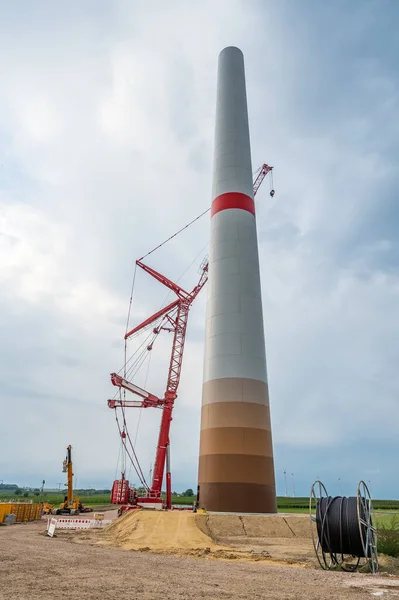 Construction site of a wind turbine with cable reel in front, crane next to the tower of the wind turbine, low angle view, cloudy day