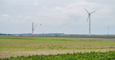 Modern renewable energy wind turbines next to wind turbine construction site, agricultural field in front, hot air balloon in background, cloudy day