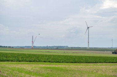 Modern renewable energy wind turbines next to wind turbine construction site, agricultural field in front, hot air balloon in background, cloudy day