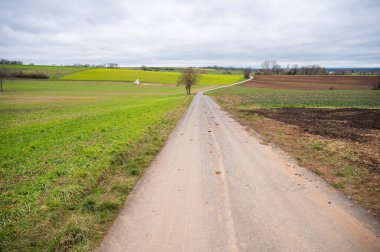 Agricultural path between multiple agricultural fields, stacked straw bale in the distance, cloudy day landscape