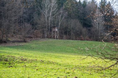 Deer stand made of wood on a hill in front of the forest, view from the distance