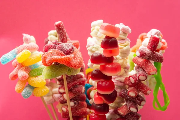 Variation of colorful fruit gums sweets skewered sour gummy bears on wooden skewers isolated on a magenta red background