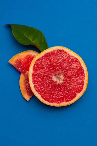 stock image Sliced sides of a grapefruit, three pieces with a green leaf, red pulp isolated on a blue background, vertical shot