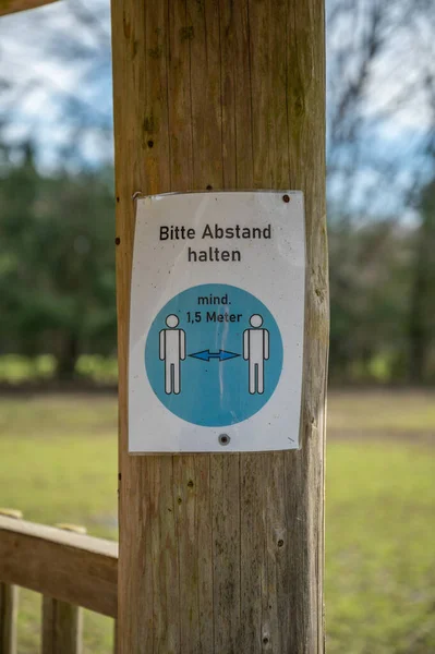 Keep distance of 1,5 meters german Corona Covid-19 Rule Sign on a tree trunk at a amusement park safari park, vertical shot